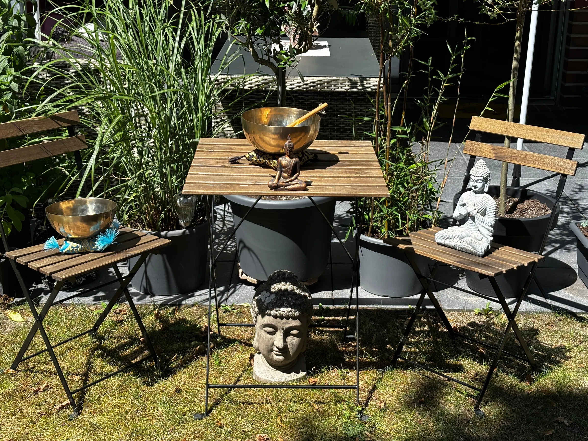 Ein Gartentisch mit Klangschalen und Buddha-Figuren, vorbereitet für eine Klangreise